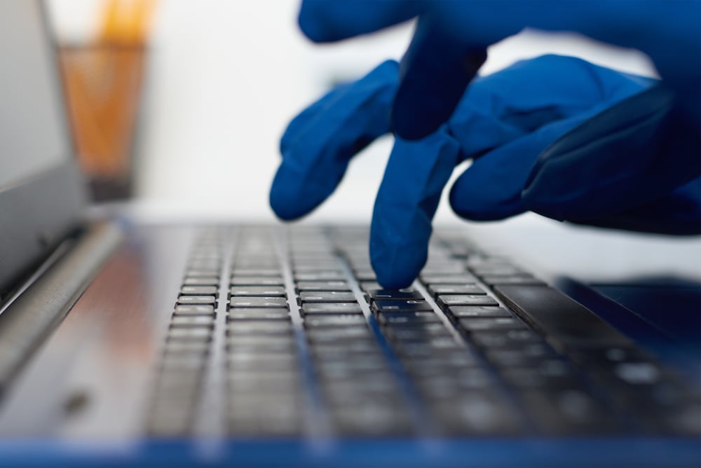 HandInProtectiveGlovesTypingOnLaptopKeyboardCyberCrime