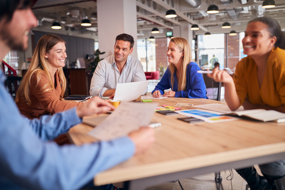 BusinessTeamHavingMeetingSittingAroundTableInModernOpen Business Team Having Meeting Sitting Around Table In Modern Open Plan Office