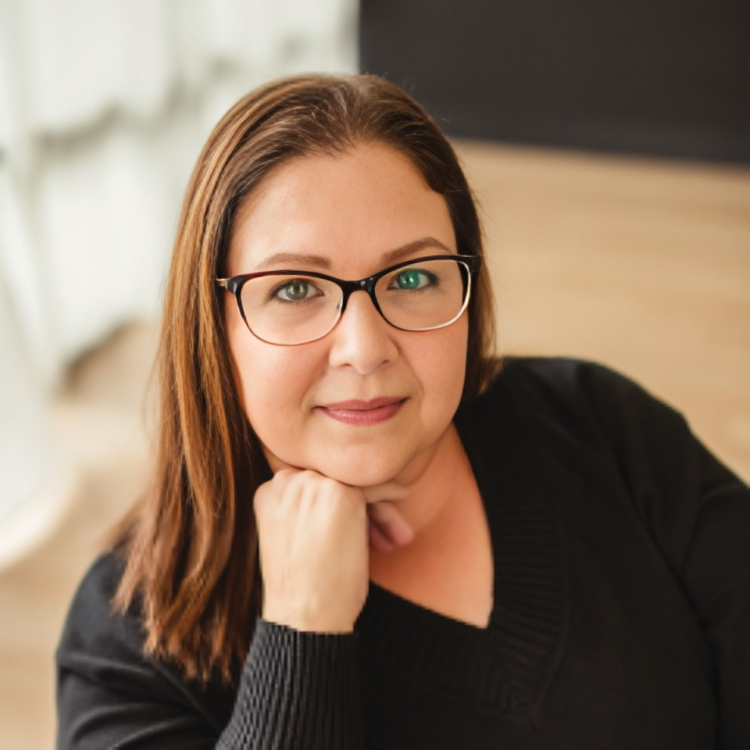 Portrait of a woman with glasses resting her chin on her hand, wearing a black sweater.