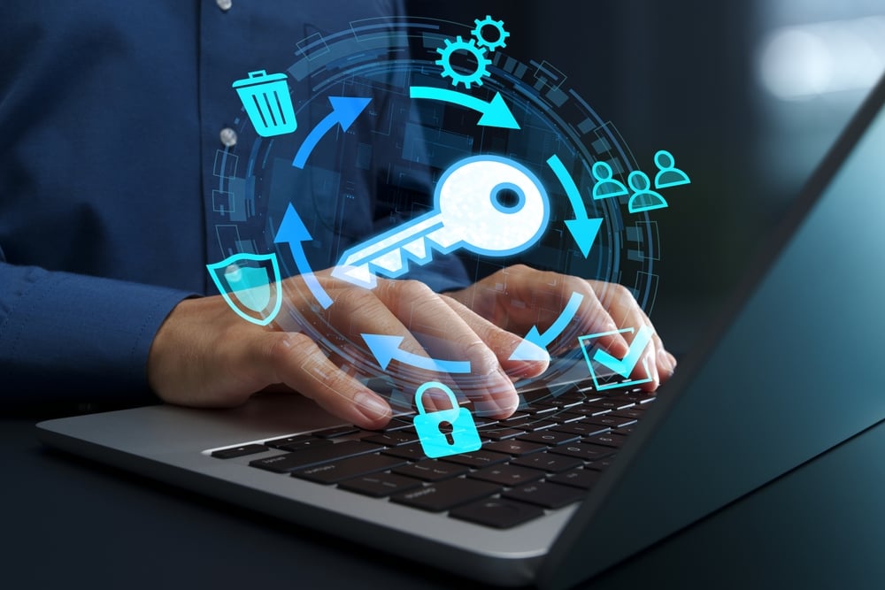 EncryptionKeyManagementSystemAndLifecycleSecureKeyExchangeAnd Person typing on a laptop with holographic security icons—key, lock, shield, and arrows representing cybersecurity.