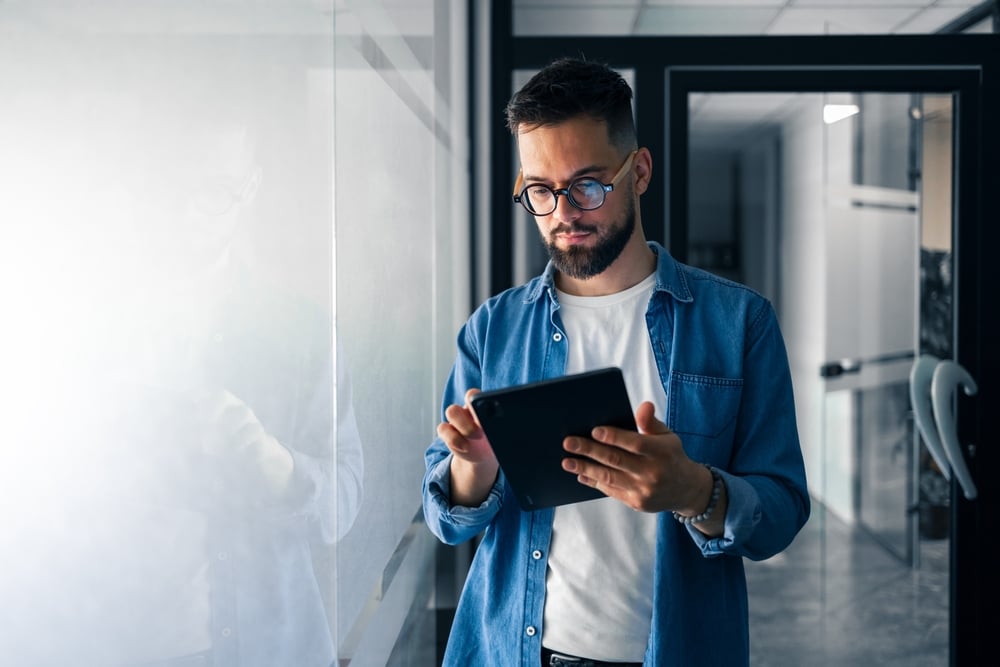 A,Focused,Professional,Wearing,Glasses,Uses,A,Digital,Tablet,In