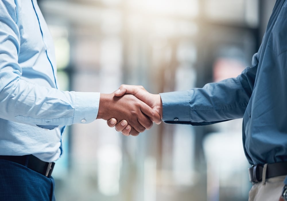 BusinessPeopleMeetingAndHandshakeCloseupForCareerProgressAgreement Two professionals in business attire shake hands in a hallway, signaling an agreement or partnership.